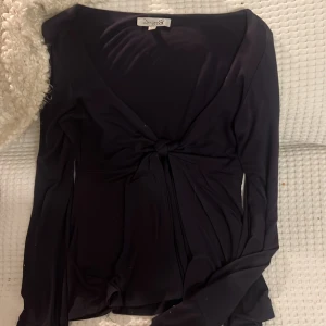 Svart långärmad topp från Design By si - Elegant svart långärmad topp från Design by si med knytning framtill. Perfekt för en stilren look.