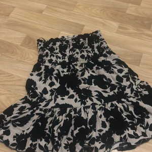 Svartvit blommig kjol från Pernilla Wahlgren - Säljer en superfin svartvit blommig kjol från Pernilla Wahlgren i storlek XS. Kjolen har en elastisk midja och volangdetaljer som ger en söt och feminin look. Perfekt för både vardag och fest! 🌸