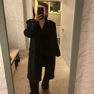 Blå kappa från Yves Saint Laurent - Säljer en elegant svart kappa från Yves Saint Laurent. Den har en klassisk design med dubbelknäppning och långa ärmar. Perfekt för höst och vinter, och ger en stilren look till alla tillfällen. Kappan är i mycket bra skick och passar perfekt för både vardag och fest.