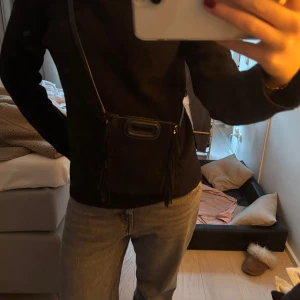 Svart axelväska med fransar - Säljer en snygg svart axelväska i mocka med coola fransdetaljer på sidorna. Väskan har ett justerbar axelrem. Perfekt för både vardag och fest! 🖤