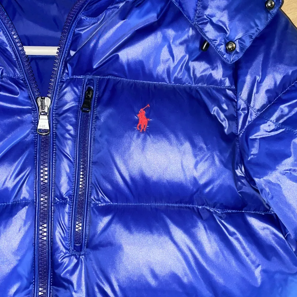 Säljer en snygg blå pufferjacka från Polo Ralph Lauren i storlek M. Jackan har en dragkedja och är långärmad med en cool röd logga på bröstet. Perfekt för kalla dagar med sin varma och vadderade design. Huvan är avtagbar och den har praktiska fickor med dragkedja. Passar perfekt för vintern! 💙kan gå ner i pris vid snabb affär skriv vid minsta fråga eller fundering. . Jackor.