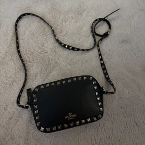 Väska Valentino - Snygg svart axelväska från Valentino med coola nitar runt kanterna. Väskan är i skinn och har en justerbar axelrem. Perfekt för både vardag och fest! 🖤 Bokstaven ”V” är lite skav på annars jättefint skick. Har tyvärr tappat bort kvittot därav priset.. 