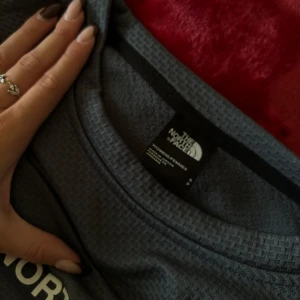 Grå tröja från The North Face - Säljer en snygg grå tröja från The North Face i mycket bra skick. Den har en normal passform och är perfekt för både vardag och träning. Tröjan är långärmad och gjord i ett bekvämt material som känns skönt mot huden. Perfekt för höst och vår!