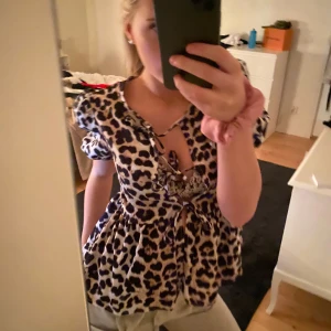 Leopardmönstrad blus med knytning - Säljer en superfin leopardmönstrad blus med knytning framtill. Den har korta ärmar och en söt volangdetalj vid ärmslut och nederkant. Perfekt för en utekväll eller fest! 🐆✨
