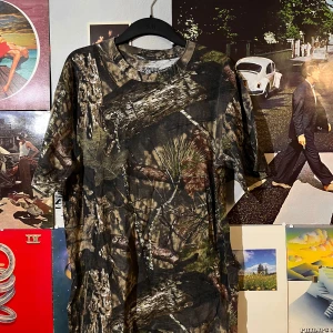 Camouflage t-shirt från Hunting Zone - Säljer en cool camouflage t-shirt från Hunting Zone i storlek XL. Perfekt för utomhusaktiviteter eller bara för en avslappnad stil. T-shirten är kortärmad och gjord i ett bekvämt material. Passar perfekt för dig som gillar att smälta in i naturen!