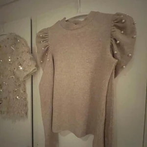 Beige tröja med puffärmar och pärlor från Zara - Säljer en superfin beige tröja från Zara med puffiga ärmar dekorerade med pärlor på axlarna. Tröjan är i bra skick och har en normal passform✨