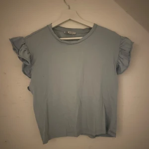 Ljusblå topp med volangärmar från Zara - Säljer en söt ljusblå topp från Zara med volangdetaljer på ärmarna. Perfekt för vår och sommar! Toppen har en rund halsringning och är i ett mjukt bomullsmaterial. Passar både till vardags och festliga tillfällen.