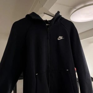 Svart hoodie från Nike - Säljer en svart hoodie från Nike i bra skick. Den har en dragkedja framtill och en klassisk Nike-logga på bröstet. Perfekt för höst och vår, med långa ärmar och en bekväm passform. Grym för både chill och träning. Denna modellen är även den gamla modellen och är därför sällsynt och säljs inte längre i nike.