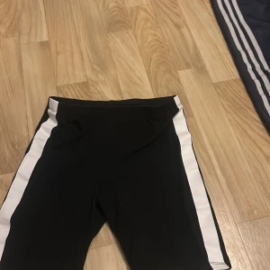 Svarta leggings med vita ränder - Säljer ett par svarta leggings med vita ränder längs sidorna. Perfekta för träning eller en avslappnad dag. De är i bra skick och har en bekväm passform. Storlek 146, vilket passar ungefär 10-11 år. Sköna och stilrena för alla tillfällen!