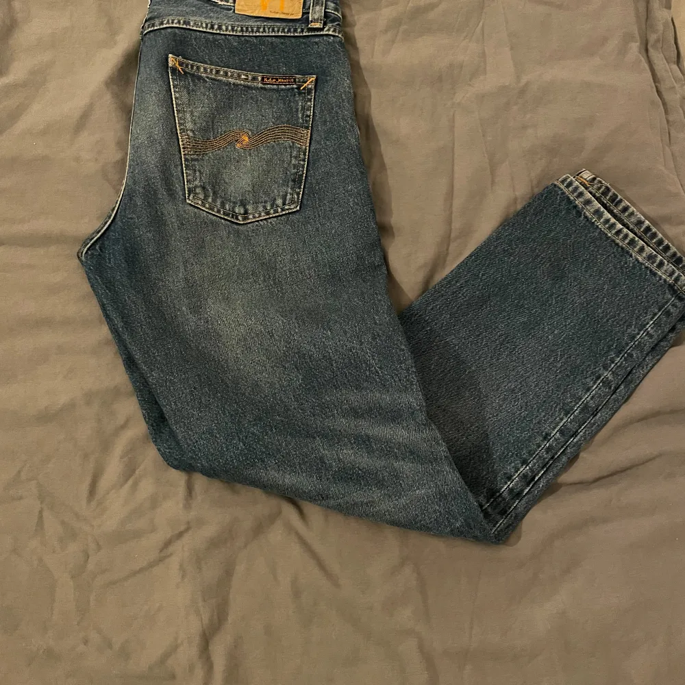 Säljer ett par klassiska blå jeans från Nudie Jeans. De har en snygg, enkel design med en bakficka som har en diskret broderad detalj. Perfekta för vardagsbruk och kan enkelt matchas med olika outfits. Passformen är normal och de är i bra skick.. Jeans & Byxor.