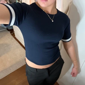 Mörkblå stickad t shirt - mörkblå ribbad topp med vita ränder på ärmarna. Toppen är kortärmad och har en tight passform som framhäver figuren. sparsamt använd! s-m