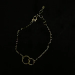 Silverfärgat armband med ringar - Snyggt och elegant armband i silverfärg med två sammanlänkade ringar, varav en är dekorerad med glittrande stenar. Armbandet är oanvänt. 💕