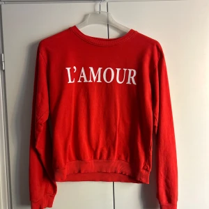 Röd tröja från Lindex med text - Säljer en cool röd tröja från Lindex med texten 'L'AMOUR' i vitt på framsidan. Tröjan är i storlek 158/164 och har långa ärmar med ribbade muddar. ❤️🥰