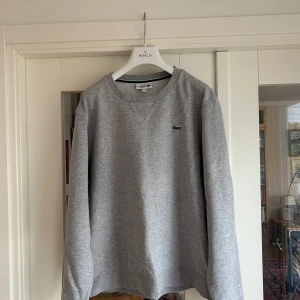 Lacoste Sport Crewneck Grå - US XL.  Mycket bra skick.  83% Bomull 17% Polyester.   Kostar 1499:- ny!   Jag är 188cm lång och den sitter aningen oversized på mig.   