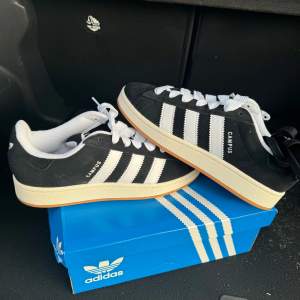 Adidas Campus 00S skor i svart med vita detaljer. Skorna är helt nya och har aldrig blivit använda och kommer med originalkartong o extra skosnören!  Nypris hos adidas cirka 1400 kr. Priset går att diskutera vid en smidig affär :)