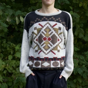  stickad tröja - Säljer en supermysig stickad tröja med ett coolt geometriskt mönster i jordnära färger som brunt, rött och beige. Perfekt för höst och vinter! Tröjan har långa ärmar och en avslappnad passform. Den är både varm och stilren, perfekt för att hålla sig snygg och bekväm i kylan.