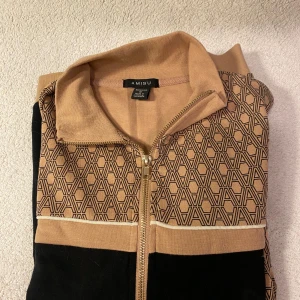 Mönstrad jacka från Amisu - Säljer en snygg jacka från Amisu i beige och svart med ett coolt geometriskt mönster. Jackan har dragkedja och långa ärmar, perfekt för höst och vår. Den är i normal passform och passar både till vardags och lite mer uppklädda tillfällen.