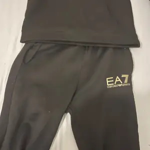 Säljer en snygg svart hoodie från Emporio Armani med deras ikoniska EA7-logga i guld på bröstet. Perfekt för en stilren och bekväm look. Tröjan har långa ärmar och en klassisk passform. Perfekt för både vardag och chill.