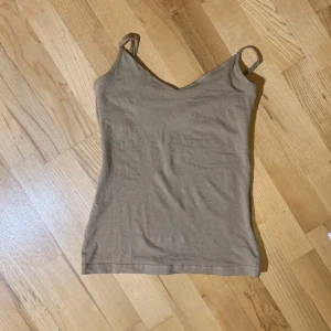 Beige linne - Säljer ett enkelt och stilrent beige linne. Linnet har en v-ringad hals och smala axelband. Det är gjort i ett mjukt och bekvämt material.