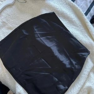 Svart satinkjol - Säljer en stilren svart kjol i kort modell. Perfekt för både vardag och festliga tillfällen. Kjolen har en enkel design utan mönster eller detaljer, vilket gör den lätt att matcha med olika toppar och accessoarer. Aldrig använd 