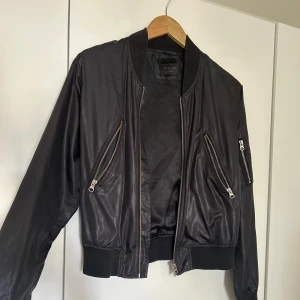 Svart bomberjacka från Tiger of Sweden Jeans - Säljer en snygg svart bomberjacka från Tiger of Sweden Jeans. Jackan har en klassisk bomberstil med dragkedjor på fickorna och en ribbad krage samt ärmslut. Perfekt för en cool och avslappnad look! Nypris 799kr