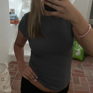 Grå tight topp - Säljer en stilren grå topp som är perfekt för vardagsbruk. Den är tight och kortärmad, vilket gör den både bekväm och snygg. Passar bra till både jeans och kjol!