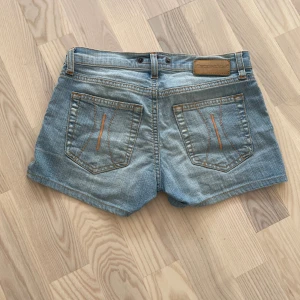 Jeansshorts i ljusblå denim - Säljer ett par snygga jeansshorts i ljusblå denim. De har en klassisk femficksdesign och är perfekt för sommardagar. Shortsen har en låg midja och är i bra skick. Perfekta för en avslappnad stil!