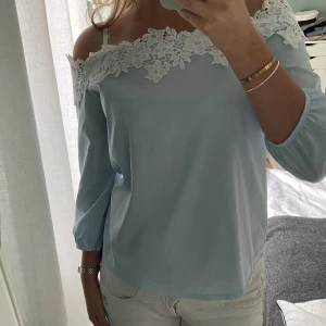 Ljusblå offshoulder topp med spetsdetaljer - Säljer en superfin ljusblå offshoulder topp med vackra vita spetsdetaljer längs kanten. Använd fåtal gånger och superfint skick❣️❣️