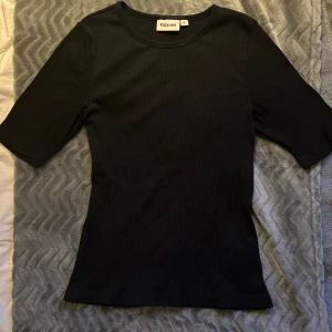 Svart ribbad topp från Kappahl - Säljer en  svart ribbad t-shirt från Kappahl!  Den har en lite mer figur sydd passform med lite längre ärmar och är perfekt för både vardag och annat🌟.  Använd några gånger, gjord av ett mjukt och bekvämt material. 