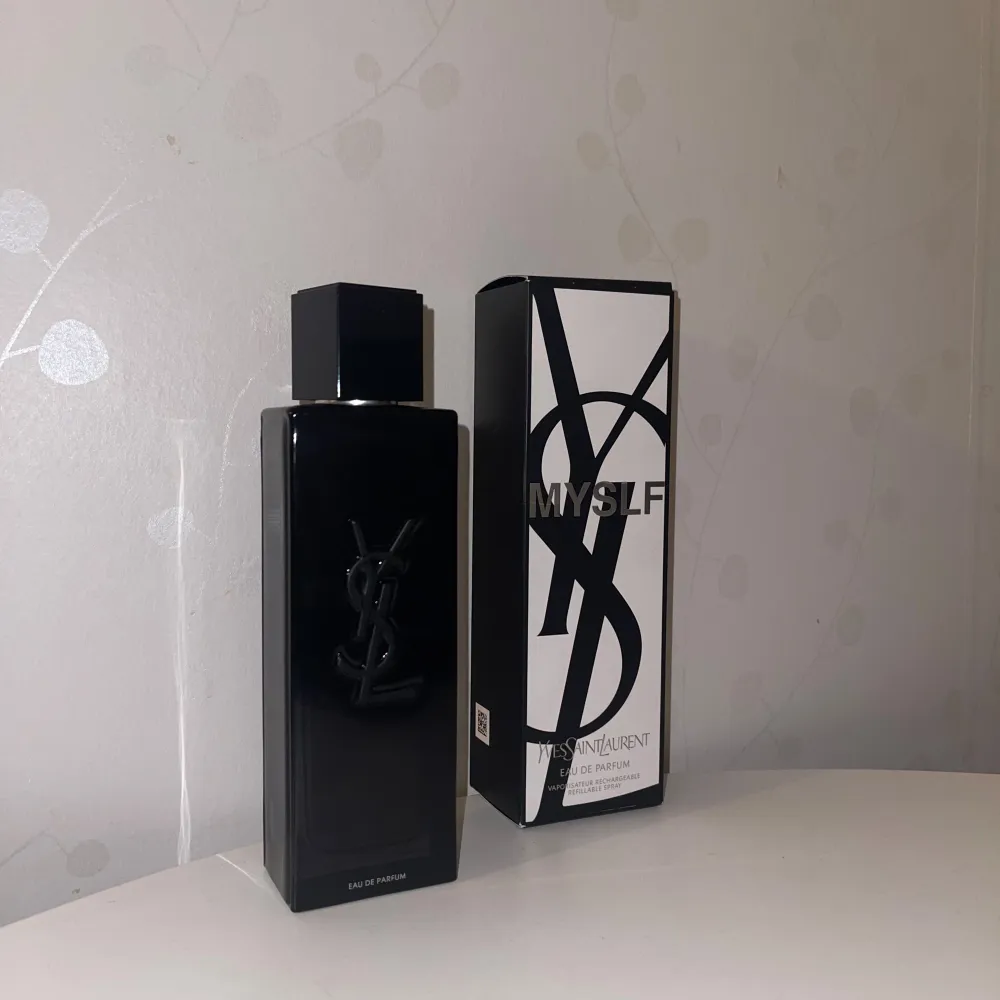 Säljer en elegant och stilren parfymflaska från Yves Saint Laurent. Flaskan är svart med en glansig finish och har den ikoniska YSL-loggan i relief på framsidan. Parfymen kommer i en snygg svartvit kartong med texten 'MYSLF'. Perfekt för den som vill ha en lyxig doftupplevelse.. Parfym.