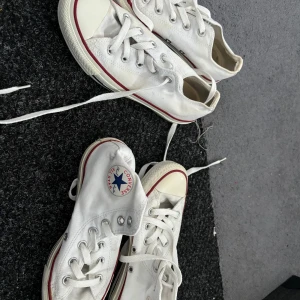 Vita Converse sneakers - Säljer ett par vita Converse sneakers i klassisk modell. De har en vit canvasöverdel med röda och blå detaljer samt den ikoniska Converse-loggan på sidan. Skorna är i välanvänt skick men fortfarande bekväma och stiliga. Perfekta för vardagsbruk!
