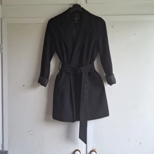 Svart kavaj från Amisu - Säljer en snygg svart blazerdress från Amisu i storlek S. Kavajen har långa ärmar och ett bälte i midjan för en figursydd passform. Perfekt för både vardag och fest! 🖤 obs har tappat knappar enligt bild 