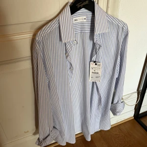 Vit och blå randig skjorta från Zara - Säljer en snygg vit och blå randig skjorta från Zara i storlek M. Skjortan är långärmad och har knappar längs hela framsidan. Perfekt för både vardag och fest! Den är i nyskick och har aldrig använts, prislappen sitter fortfarande kvar. Materialet känns som bomull och är väldigt bekvämt. ❗️❗️om du vill veta nåt, fler bilder, förhandla pris, skriv ba👍👍skjortan sitter avslappnat och har en tidlös silhuett.⭐️