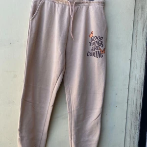 Beige mjukisbyxor från FB Sister - Säljer ett par superbekväma beige mjukisbyxor från FB Sister i storlek XL. De har en elastisk midja med snörning och ett tryck med texten 'Good Things Are Coming' tillsammans med fjärilar på ena benet. Perfekta för en chill dag hemma eller en avslappnad promenad. 🦋
