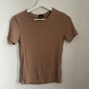 Säljer en snygg beige ribbad topp från Gina Tricot. Den har en tight passform och korta ärmar, perfekt för både vardag och fest. Toppen är i storlek S och är i nyskick. Passar bra till jeans eller kjol för en stilren look!