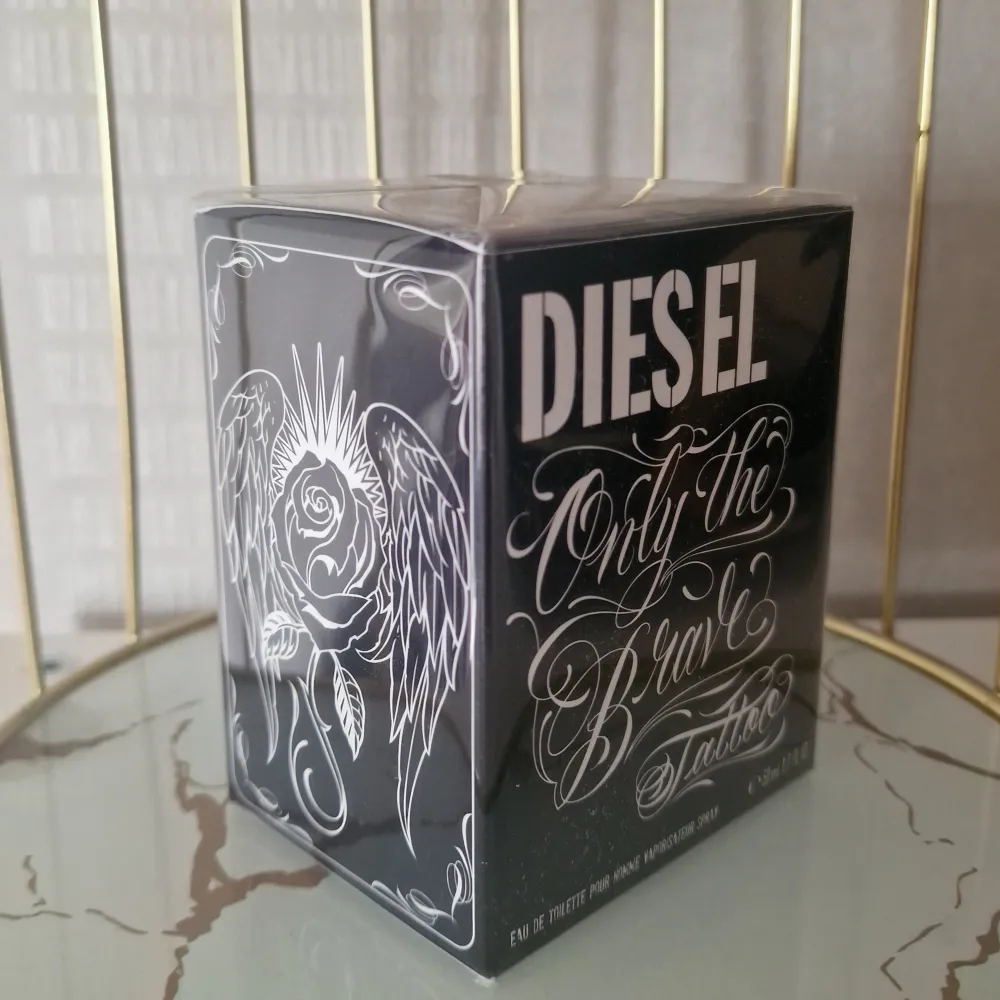 Säljer en cool parfym från Diesel, 'Only the Brave Tattoo'. Den kommer i en snygg svart förpackning med vita tatueringsinspirerade mönster och text. Flaskan innehåller 50 ml av denna doft som är perfekt för den modiga och självsäkra personen. Perfekt present eller för att unna sig själv något extra!. Parfym.