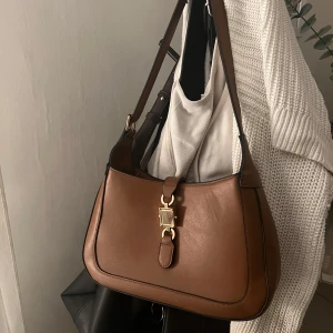 Brun väska - Superfin, rymlig axelväska med guldigt knäppe. Dragkedja och innerficka. Justerbart axelband. Den enda defekten är att jag gjort ett extra hål i axelbandet så den skulle bli aningen kortare. Säljs inte längre på glitter 💖