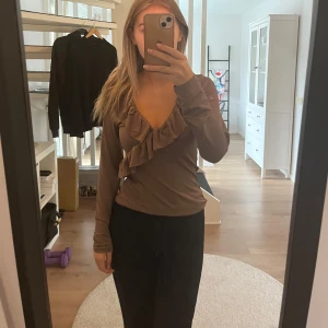Brun omlottopp med volangdetaljer - Säljer en superfin brun omlottopp med volangdetaljer. Den har långa ärmar och en snygg v-ringning. Perfekt för höst och vår, och funkar både till vardags och fest. Passar bra med jeans eller kjol! Prislappen är kvar