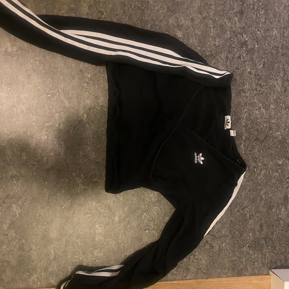 Säljer en svart långärmad tröja från Adidas med vita ränder längs ärmarna. Perfekt för en sportig look eller avslappnad stil. Tröjan är i mycket bra skick.. Tröjor & Koftor.