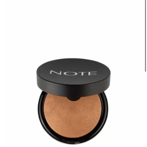 Baked Blusher från Note Cosmetique (Helt nytt aldrig använt och oppönad) - Snygg baked blusher från Note Cosmetique med macadamiaolja, perfekt för alla hudtyper. Den har en varm, glödande nyans som ger ansiktet en fräsch och strålande look. Kommer i en stilren svart förpackning.