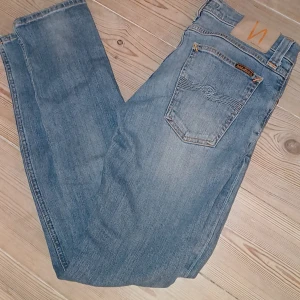 Blå jeans från Nudie Jeans - Säljer ett par klassiska blå jeans från Nudie Jeans i storlek W29L32. De har en snygg, sliten look med orange sömmar och en bekväm passform. Perfekta för både vardag och fest! 🕺👖