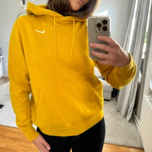 Gul hoodie från Nike - Säljer en superfin gul hoodie från Nike. Den har en klassisk passform med en stor ficka fram och justerbar huva. Perfekt för höst och vår när du vill vara både bekväm och stilren. Den ikoniska Nike-loggan syns tydligt på bröstet. Passar perfekt till vardags eller träning!