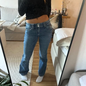 Blå bootcut jeans - Säljer ett par snygga blå bootcut jeans i mycket bra skick. De är lågmidjade och har en klassisk femficksdesign med knappar och dragkedja framtill. 