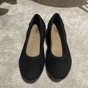 Svarta ballerinaskor - Säljer ett par svarta ballerinaskor som var för små för mig och därför inte kom till någon användning, nyskick. De är perfekta för både vardag och festliga tillfällen. Skorna har en enkel och stilren design med rund tå och en bekväm sula. Passar perfekt till både jeans och klänning! De har ett litet sträck som bara syns med blixt. Vet inte vart de är ifrån då de va länge sedan jag köpte dom🥰