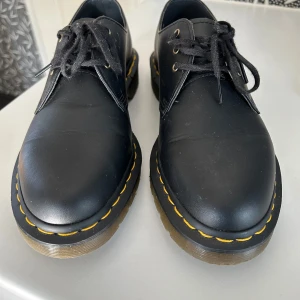 Dr Martens - Säljer ett par klassiska svarta Dr. Martens i skinn med den ikoniska gula sömmen. Skorna har snörning och en robust sula som ger bra grepp. Perfekta för både vardag och fest! De är i mycket bra skick och redo för nya äventyr. Storlek 42. 