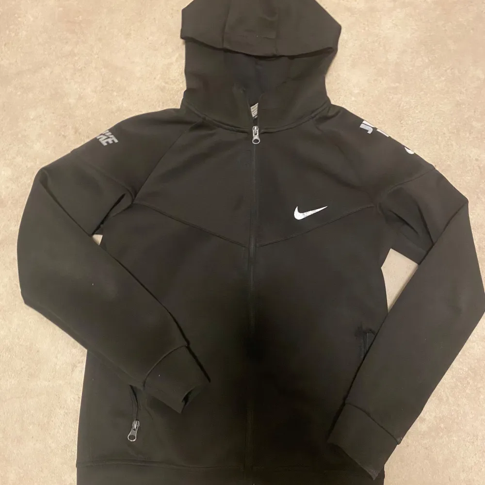 Säljer en svart hoodie från Nike i mycket bra skick. Den har en dragkedja framtill och en klassisk Nike-logga på bröstet. Perfekt för både träning och vardag.. Tröjor & Koftor.