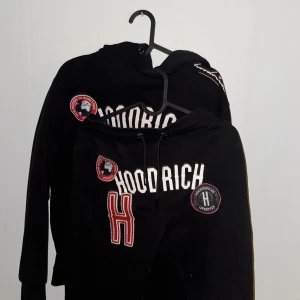 Svart hoodie och byxor från Hoodrich - Säljer en svart hoodie och matchande byxor från Hoodrich. Setet har coola tryck och broderade detaljer i vitt och rött. Perfekt för en avslappnad och stilren look. Hoodien har en klassisk passform med långa ärmar och byxorna har en bekväm resår i midjan. Hoodien är i storlek XS & byxorna i storlek S