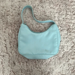 Ljusblå axelväska från Monki - Säljer en söt ljusblå axelväska från Monki. Den har en enkel design med dragkedja upptill och är perfekt för vardagsbruk. Väskan är i bra skick och passar till både vår och sommaroutfits. Perfekt för att bära dina nödvändigheter med stil! 💙