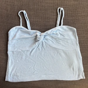 Ljusblå ribbad linnetopp - Säljer en söt ljusblå ribbad linnetopp med smala axelband och en knutdetalj framtill. Perfekt för sommardagar eller som ett lager under en kofta. Toppen är i bra skick och superbekväm att bära. Passar perfekt till jeans eller shorts! Passar M-L