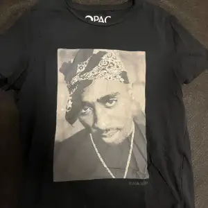 Svart 2pac T-shirt med hans ansikte på framsidan och handskriven text på baksidan med ett budskap. Jätte cool tröja men säljer för att den inte är min stil längre.